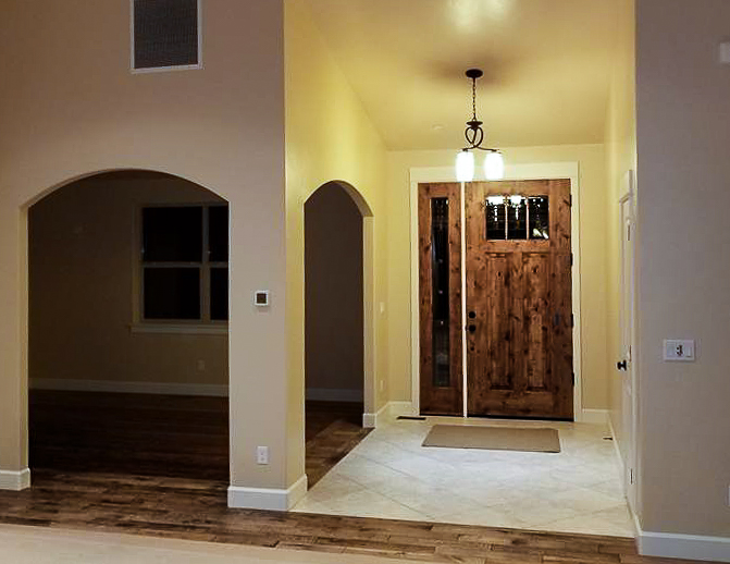 Finished interior entryway repaint, warm tan walls with a stained wood door and arched openings