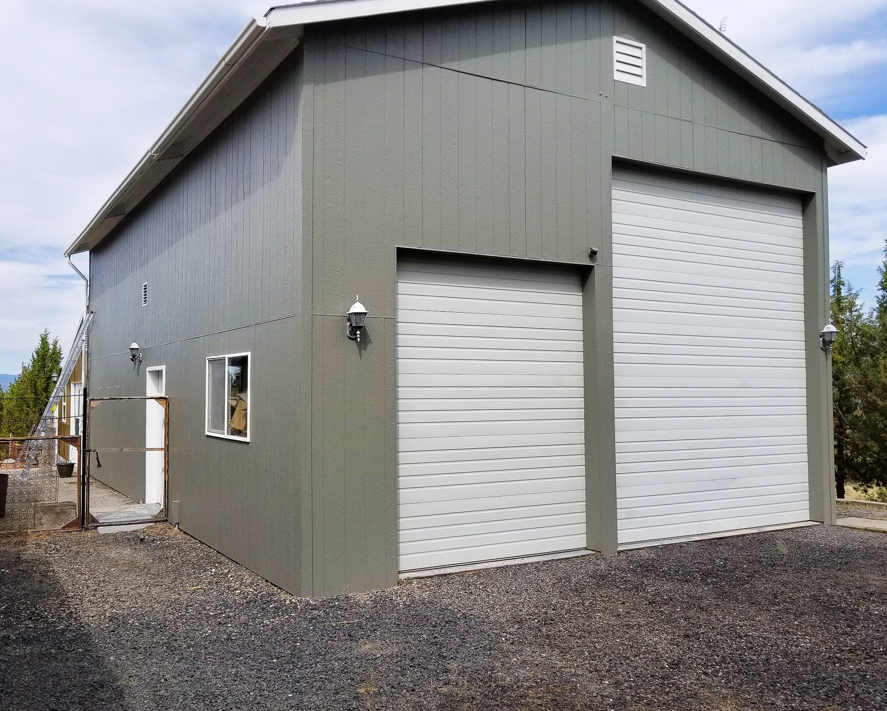 Finished exterior repaint of a gray pole barn and shop building with white garage doors